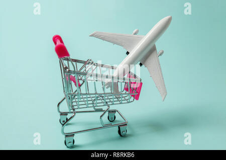 Miniature toy model plane, supermarket grocery push cart for shopping on blue pastel colorful paper trendy background. Sale travel by plane weekend se Stock Photo