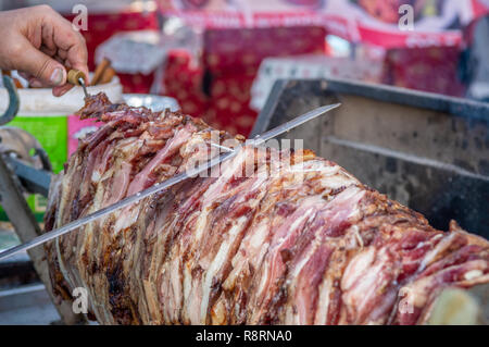 Turkish Cag Kebab cooking in a BBQ. Cook slicing the meat with a knife. Stock Photo
