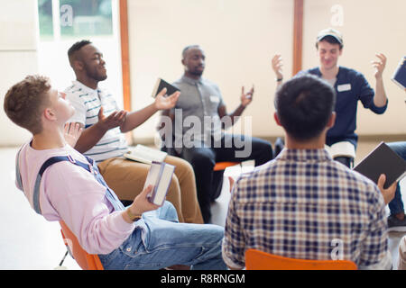 Men with bibles praying with arms outstretched in prayer group Stock Photo