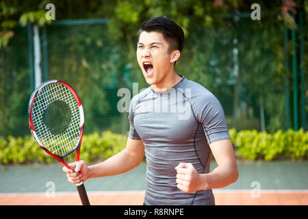 young asian male tennis player celebrating after scoring a point Stock Photo