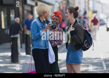 Young women friends with camera on urban sidewalk Stock Photo