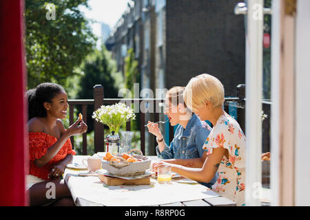 Young women friends eating brunch on sunny apartment balcony Stock Photo