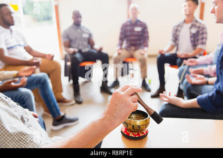 Man using singing bowl in meditation group Stock Photo