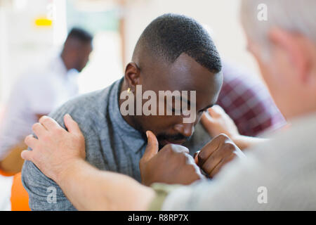 Man comforting young man in group therapy Stock Photo