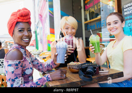 Portrait smiling young women friends drinking smoothies at sidewalk cafe Stock Photo