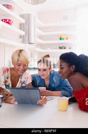 Young women friends using digital tablet at kitchen table Stock Photo