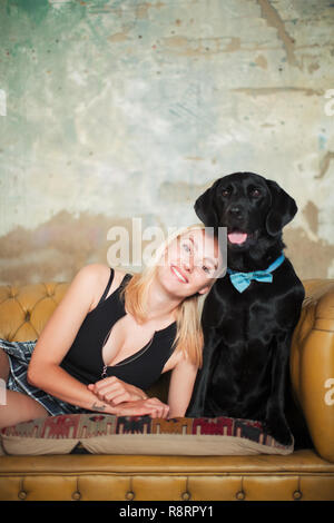 Portrait smiling, carefree young woman with black dog wearing bow tie on sofa Stock Photo