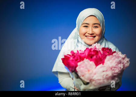 Portrait smiling, confident young woman in hijab holding pink peonies Stock Photo