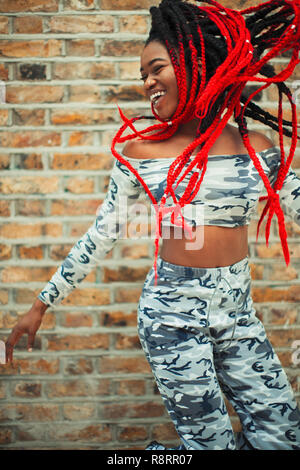 Carefree young woman in camouflage clothing dancing against brick wall Stock Photo