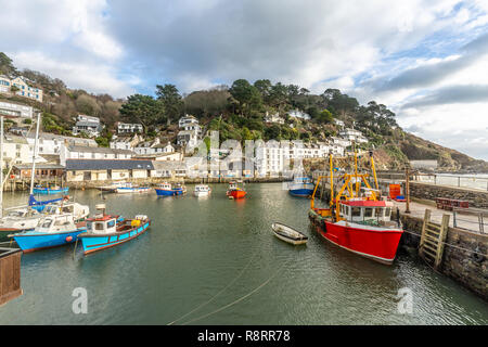 Red and Blue fishing boats moored at Polperro Harbour, Cornwall, with view of white cottages and open sea. Stock Photo