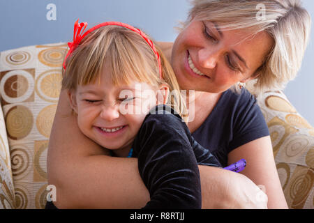 Fun happy loving mother and daughter enjoying a laugh and cuddle as the relax together in a comfortable armchair at home Stock Photo