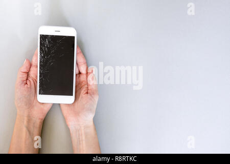 Smartphone with broken screen in hand on grey background Stock Photo