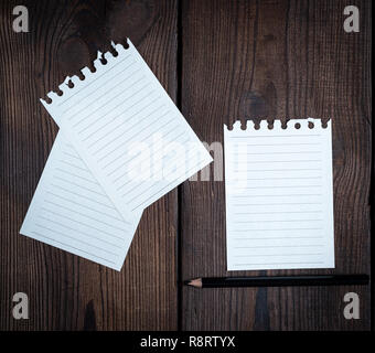 empty white sheets in a line torn out of notepad on a brown wooden background Stock Photo