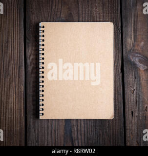 notebook on a black iron spring with brown empty sheets on a brown wooden background, close up Stock Photo