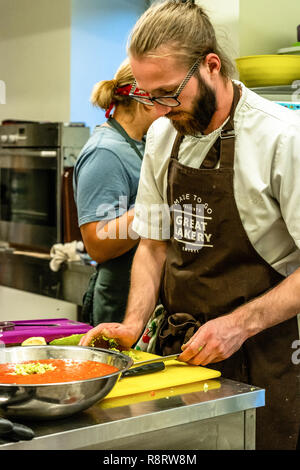 Male Chef Slicing Avocado for  Wedding Meal - Kitchen Set, Text on Apron "Made to go presents, Great Bakery, Enjoy" Stock Photo