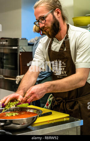 Male Chef Slicing Avocado for  Wedding Meal - Kitchen Set, Text on Apron "Made to go presents, Great Bakery, Enjoy" Stock Photo