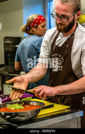 Male Chef Slicing Avocado for  Wedding Meal - Kitchen Set, Text on Apron "Made to go presents, Great Bakery, Enjoy" Stock Photo