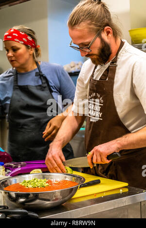 Male Chef Slicing Avocado for  Wedding Meal - Kitchen Set, Text on Apron "Made to go presents, Great Bakery, Enjoy" Stock Photo