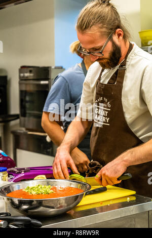 Male Chef Slicing Avocado for  Wedding Meal - Kitchen Set, Text on Apron "Made to go presents, Great Bakery, Enjoy" Stock Photo