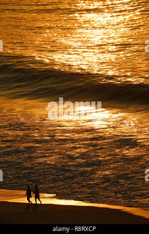 Atlantic ocean in golden morning sunlight reflections with silhouette of two people walking on Copacabana beach, Rio de Janeiro, Brazil Stock Photo