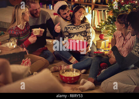 Funny young people are sharing gifts with Christmas decorations and a beautiful Christmas tree. Concept of celebration Christmas and new year. Stock Photo