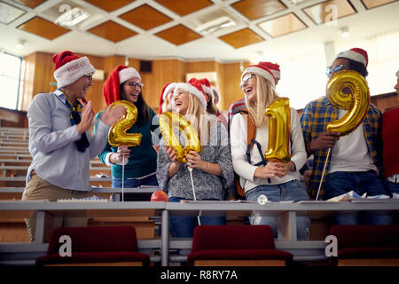 Group of happy colleagues in Santa hat having fun at new year celebration on university Stock Photo