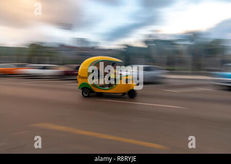 Cuban woman driving a speeding bright yellow Coco Taxi in Havana Cuba Stock Photo