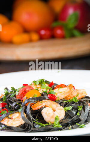 Black squid ink Fettuccine pasta with prawns or shrimps cherry tomatoes, parsley, chili in wine and butter sauce. Stock Photo
