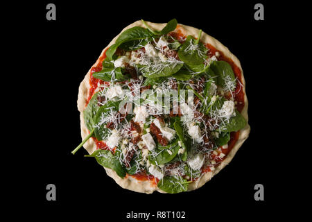 Raw uncooked pizza with spinache dried tomatoes and feta cheese on black background. Stock Photo