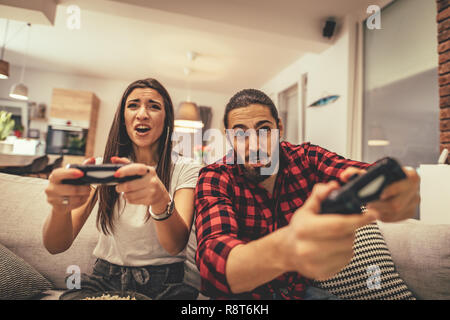 Excited couple is playing video games at home sitting on sofa. They have great weekend in nice company indoors. Stock Photo