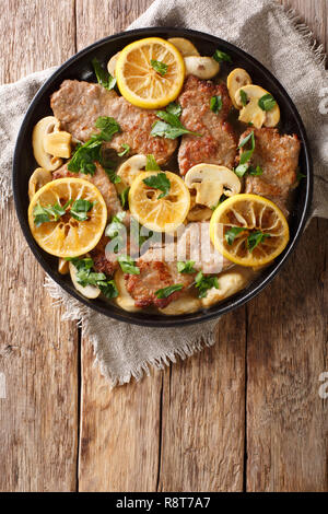 Tasty Italian fillet of veal scaloppini with mushrooms and lemons in sauce close-up in a frying pan on the table. Vertical top view from above Stock Photo