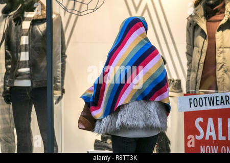 Preston, Lancashire, UK  Weather. Dec 2018. Wet & windy day for Christmas shoppers forcing woman to take cover under a multi-coloured striped blanket from the heavy rain.  Credit; MediaWorldImages/AlamyLiveNews Stock Photo