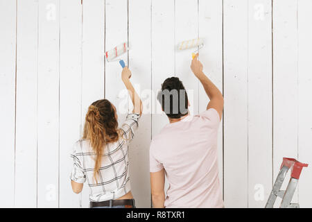 Photo of caucasian couple man and woman painting white wall and making renovation using paint rollers Stock Photo
