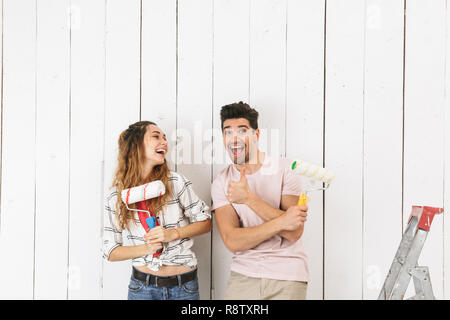 Photo of european couple man and woman painting white wall and making renovation using paint rollers Stock Photo