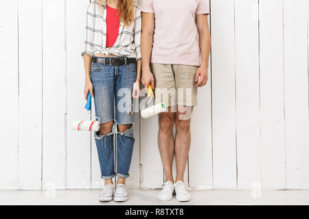 Cropped photo of amusing couple man and woman painting white wall and making renovation using paint rollers Stock Photo