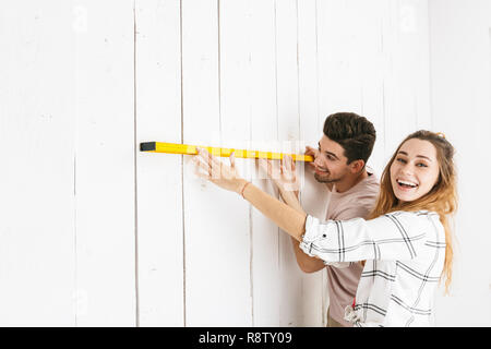 Photo of attractive couple man and woman holding big ruler at white wall while measuring and making renovation indoor Stock Photo