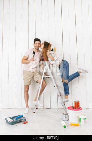 Full length photo of beautiful couple man and woman standing on ladder while painting white wall and making renovation indoor Stock Photo