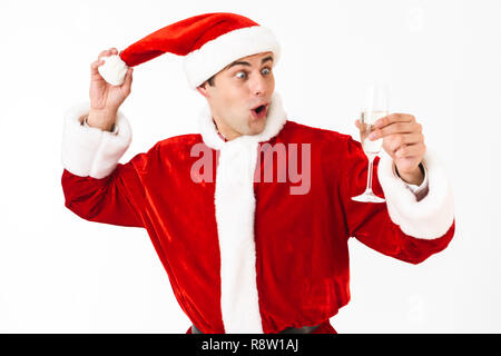 Portrait of surprised man 30s in santa claus costume and red hat drinking champagne from glass isolated over white background in studio Stock Photo