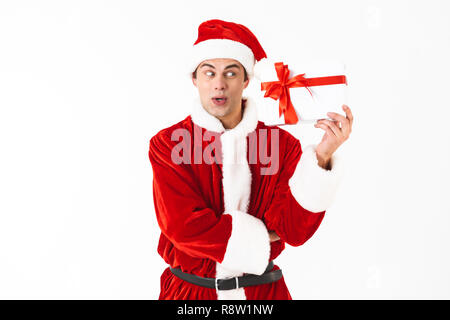 Portrait of emotional man 30s in santa claus costume and red hat holding present box isolated on white background in studio Stock Photo