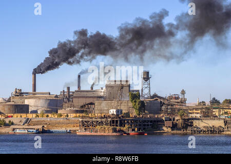Climate change, global warming: Egyptian sugar factory on the River Nile belching out billowing thick black dirty smoke and fumes from its chimneys Stock Photo