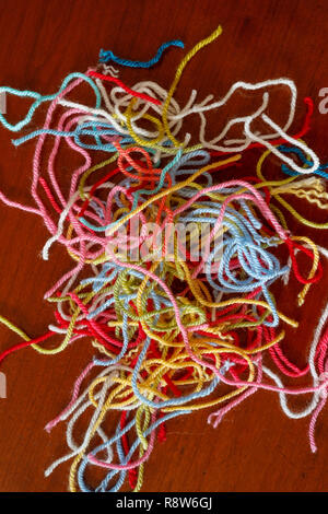 Pile of left over lengths of multi-coloured threads of cut threads of wool in warm pastel colours on a wooden table Stock Photo