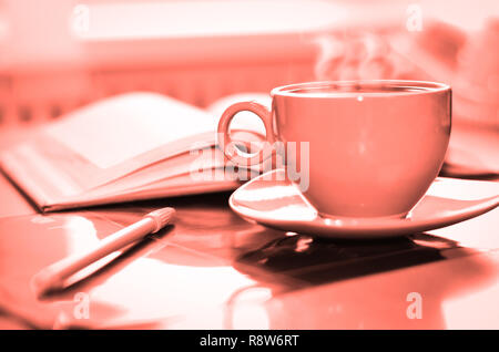 Living coral color of the Year 2019. Cup of coffee on the desk in the office. Retro toned Stock Photo