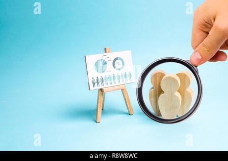 Magnifying glass is looking at the People stand near the canvas with graphs and reports. Business report, summary and planning. Market research and an Stock Photo