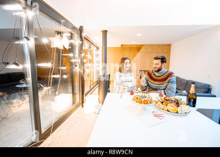 Young couple having festive dinner sitting together in the modern house during the winter holidays. Wide interior view Stock Photo