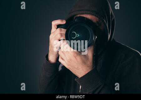 Hooded photographer behind DSLR camera, low key portrait Stock Photo