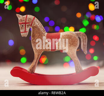 A Rocking horse with christmas lights on wooden table.
