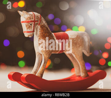 A Rocking horse with christmas lights on wooden table.