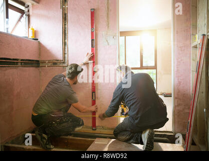 Construction workers using level too and tape measure in house Stock Photo