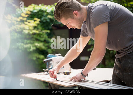 Construction worker measuring wood in driveway Stock Photo