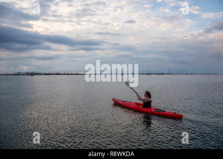 Adventurous girl kayaking in the Atlantic Ocean during a vibrant cloudy sunset. Taken in Key West, Florida Keys, United States. Stock Photo